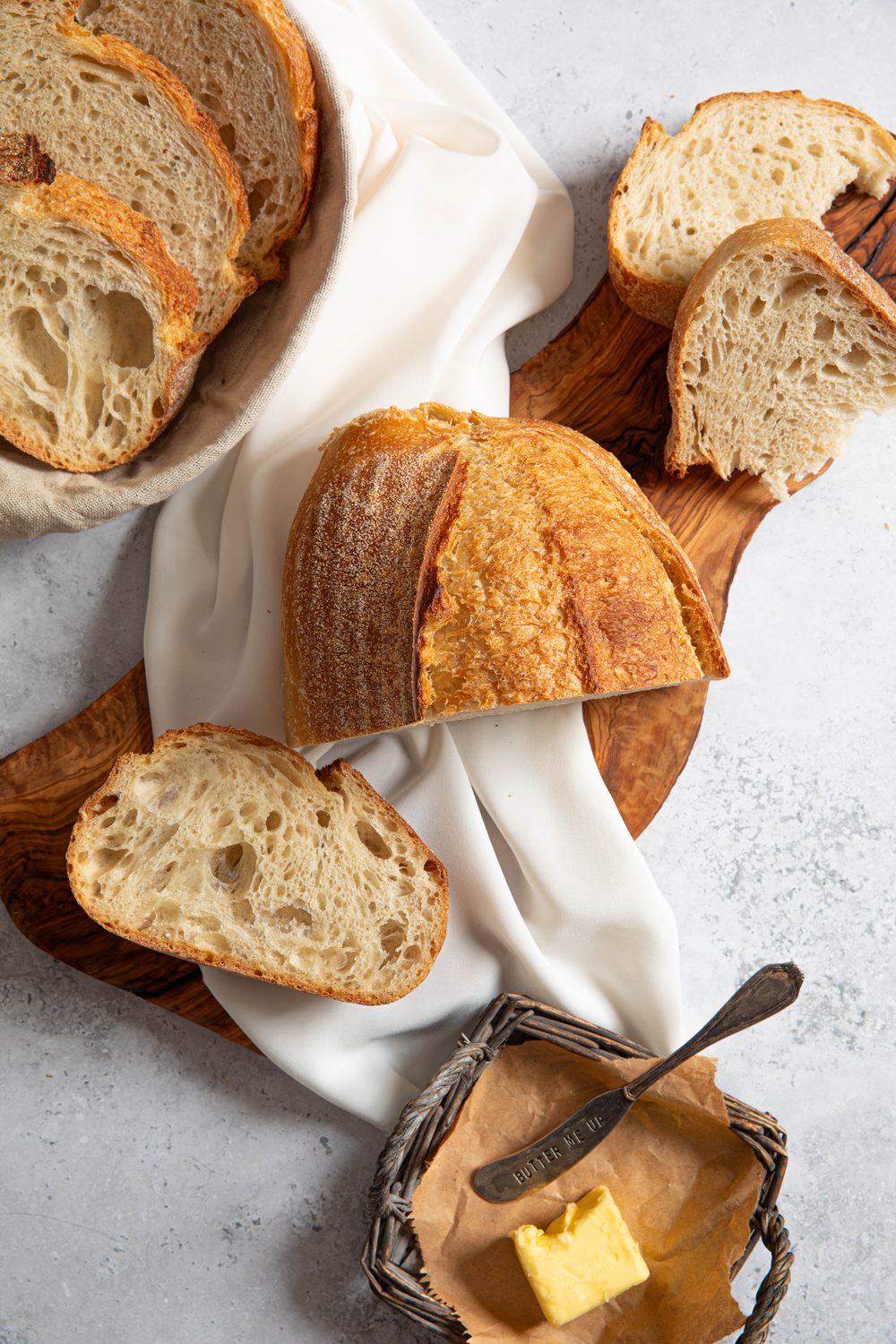 Sliced sourdough loaves on a board and linen cloth with a basket of butter