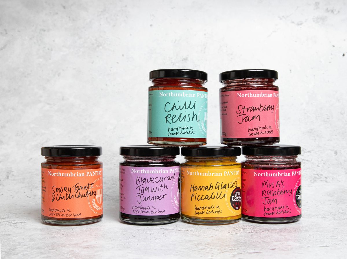 A stack of six jars of handmade jams, chutney, relish and piccalilli with brightly coloured labels
