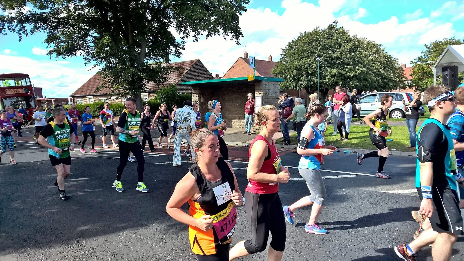 Runners in charity vests along a South Shields street on Great North Run day, one of them wearing a full white Elvis jumpsuit