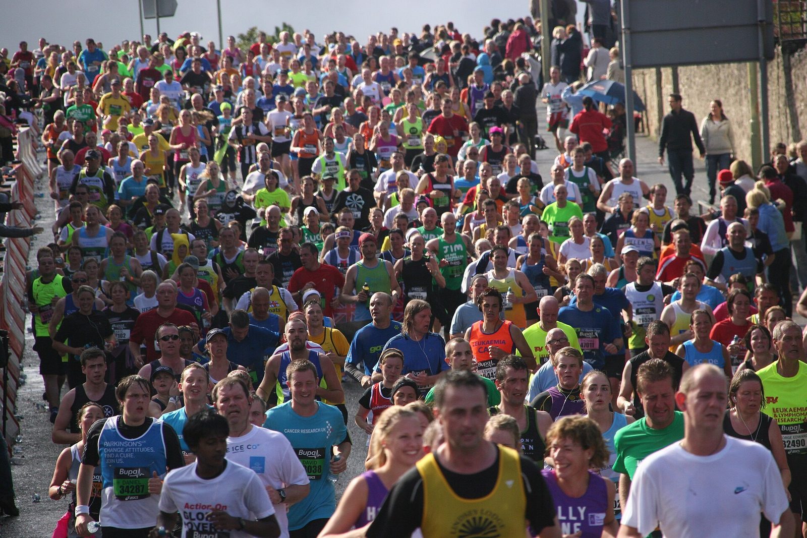 A dense crowd of runners in charity vests and running tops filling the full width of a road in bright sunshine on the Great North Run