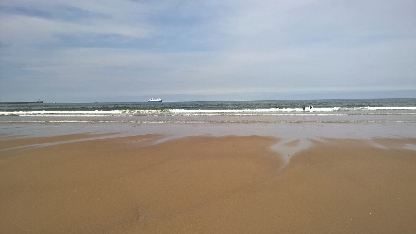 Wide wet sands and the open water of the North Sea at South Shields, with a ship on the horizon under a pale sky