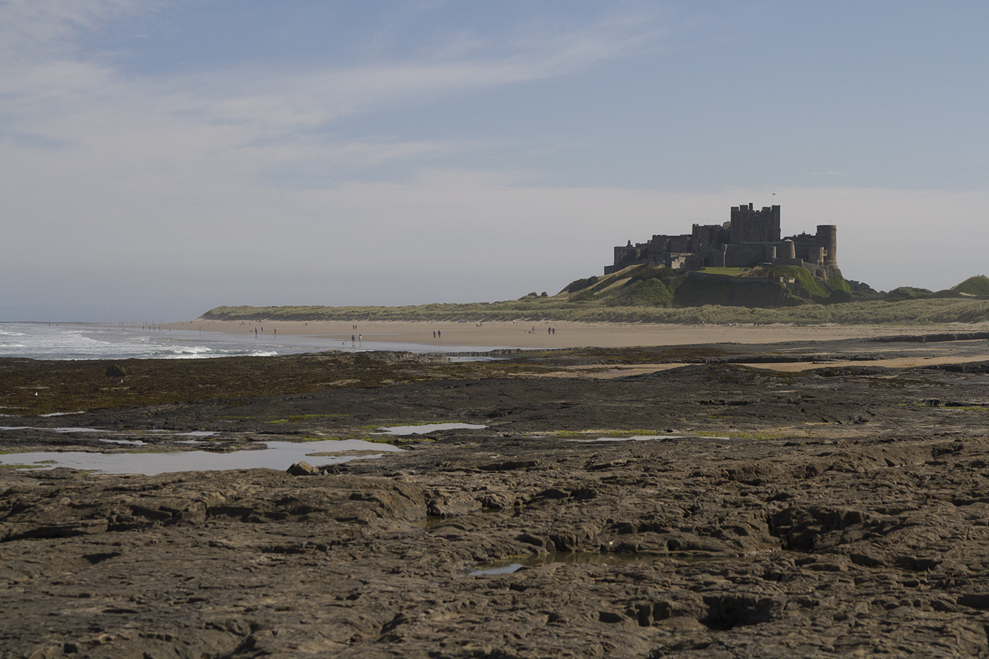 Bamburgh Castle seen across the rocks and golden sands of Bamburgh Beach on a summer's day