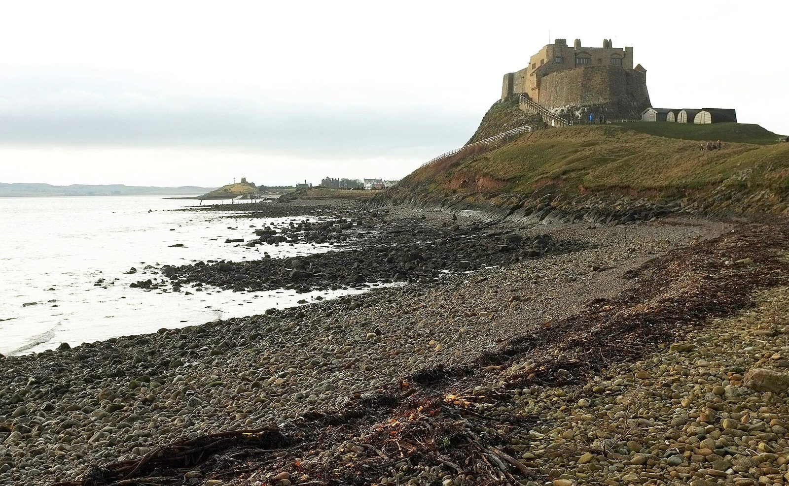 Lindisfarne Castle standing on its crag above the stony shore of Holy Island, with the sea and the mainland beyond